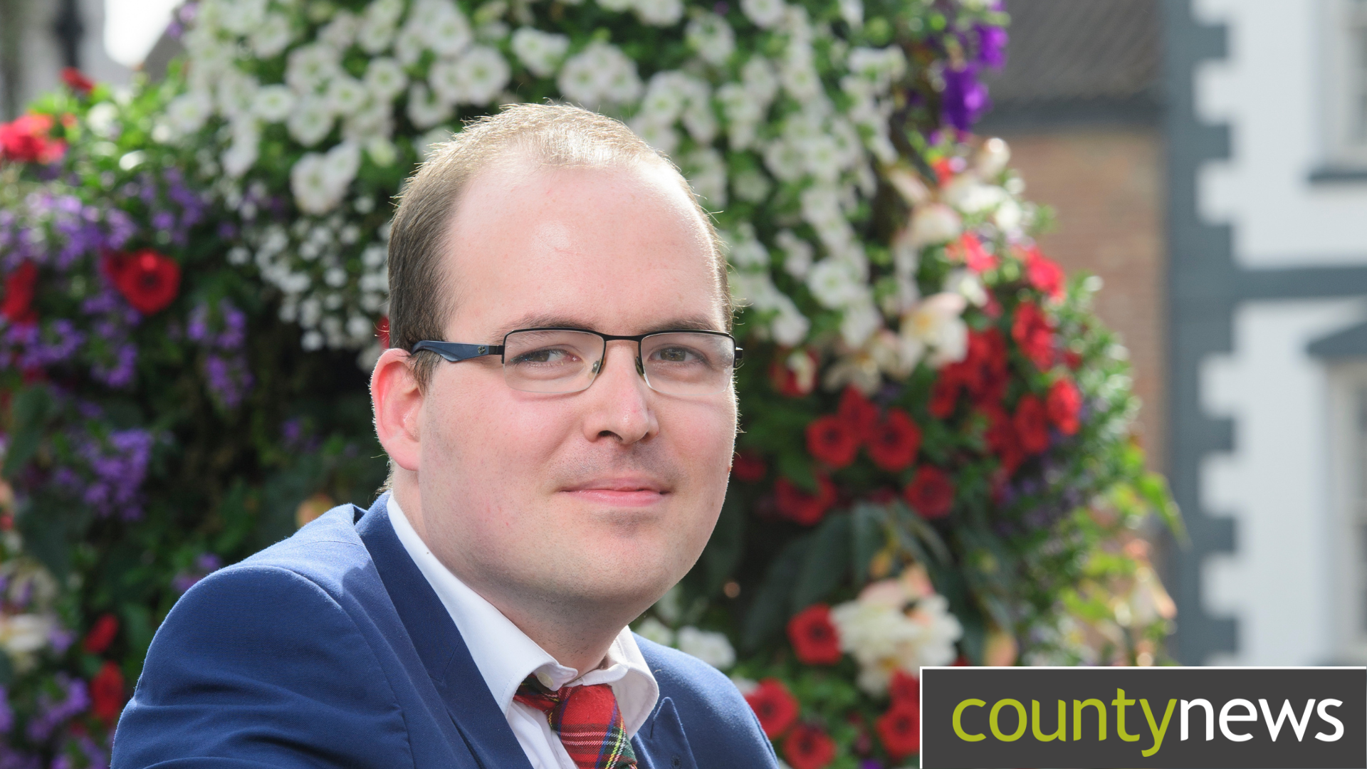 Cllr Tom Smith poses for the camera, with flowers behind him.