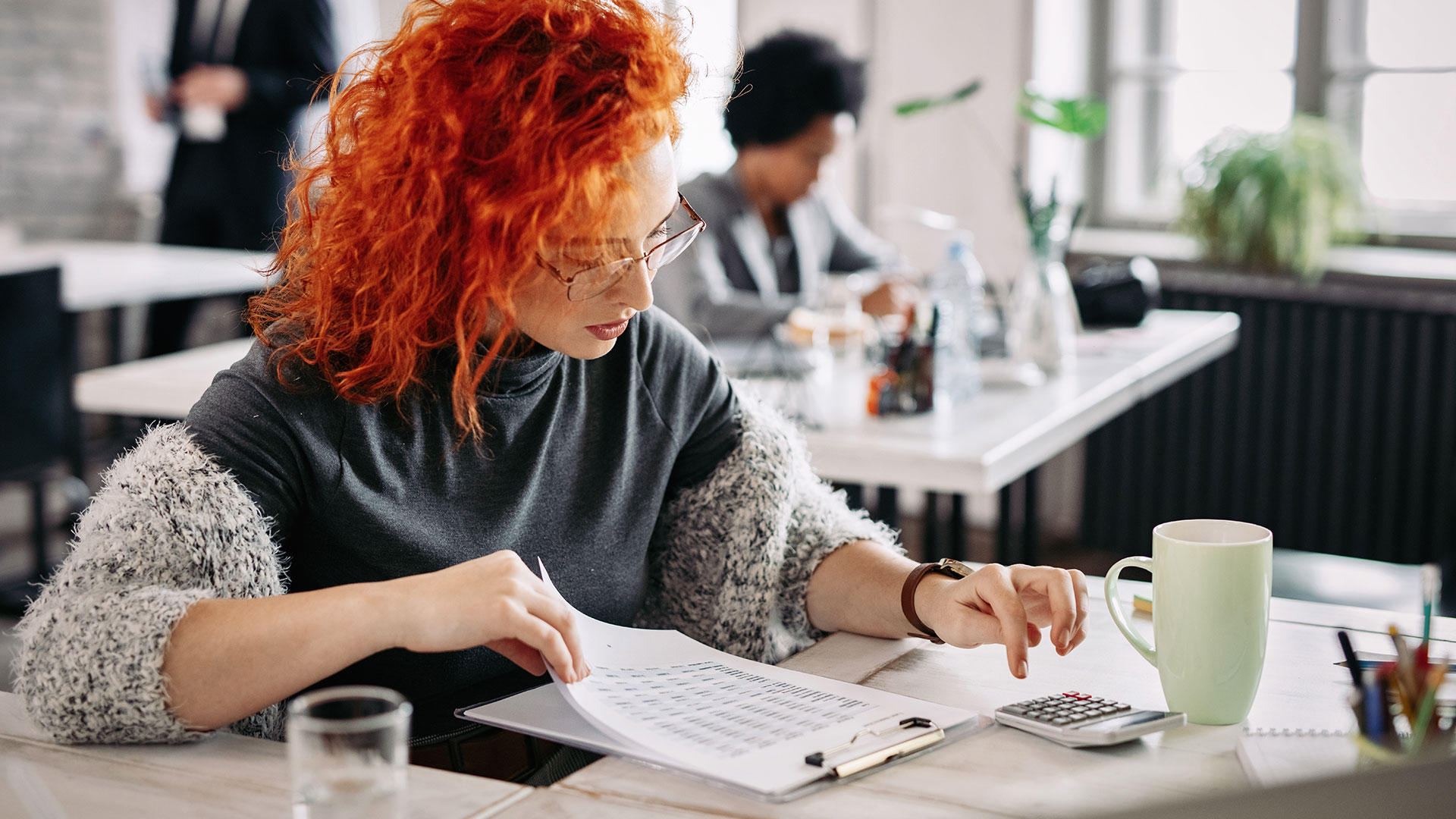 Redheaded woman sitting at a desk using a calculator