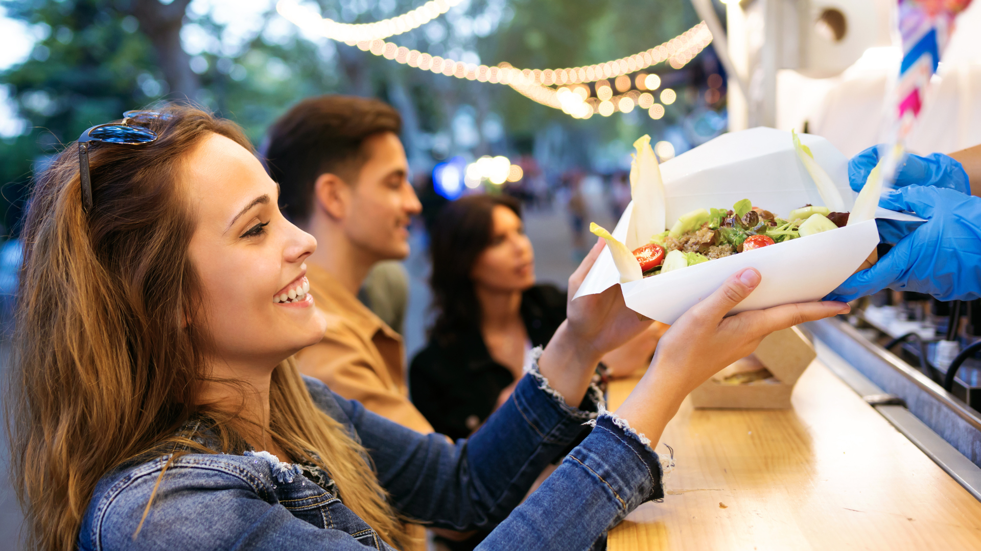 A lady collecting food from a street food stall with people and festoon lights in the background