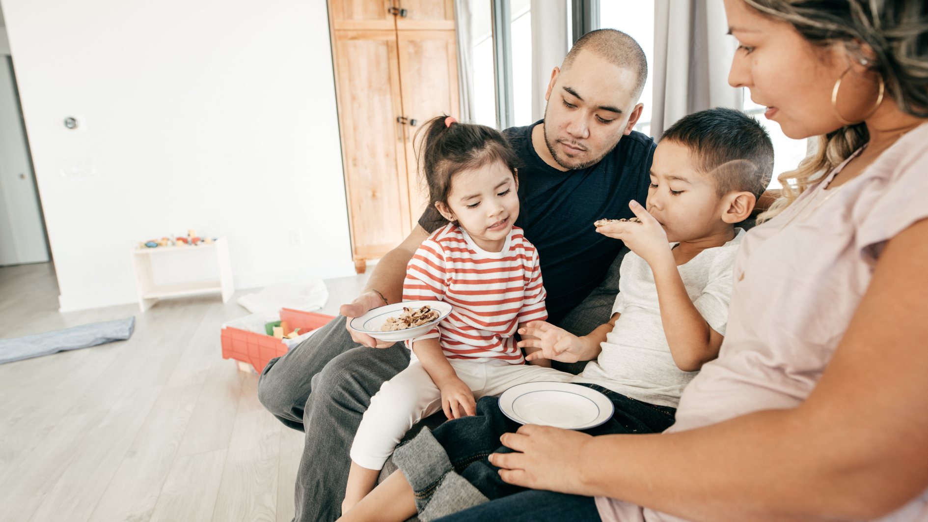 Two parents sat on a sofa with a young girl and boy on their knees talking together