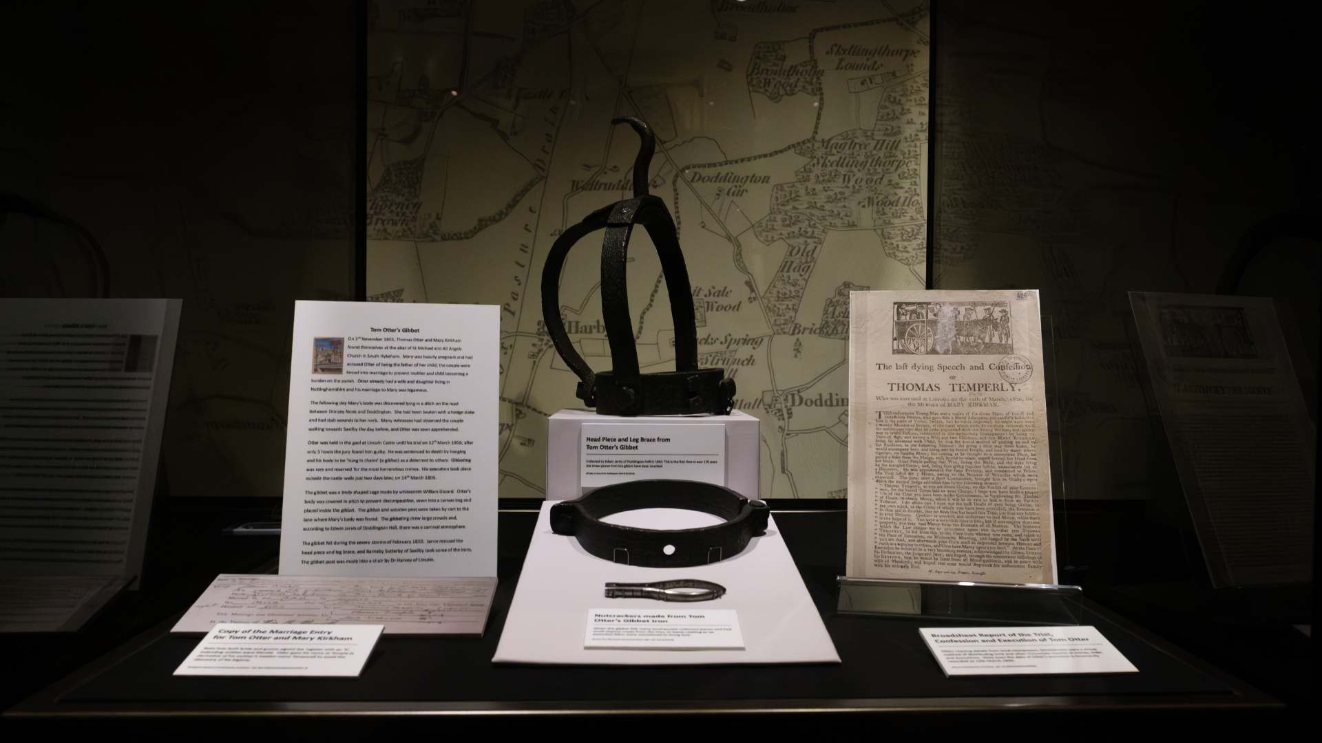 Artefacts of a metal gibbet and documentation in a glass museum case in low light