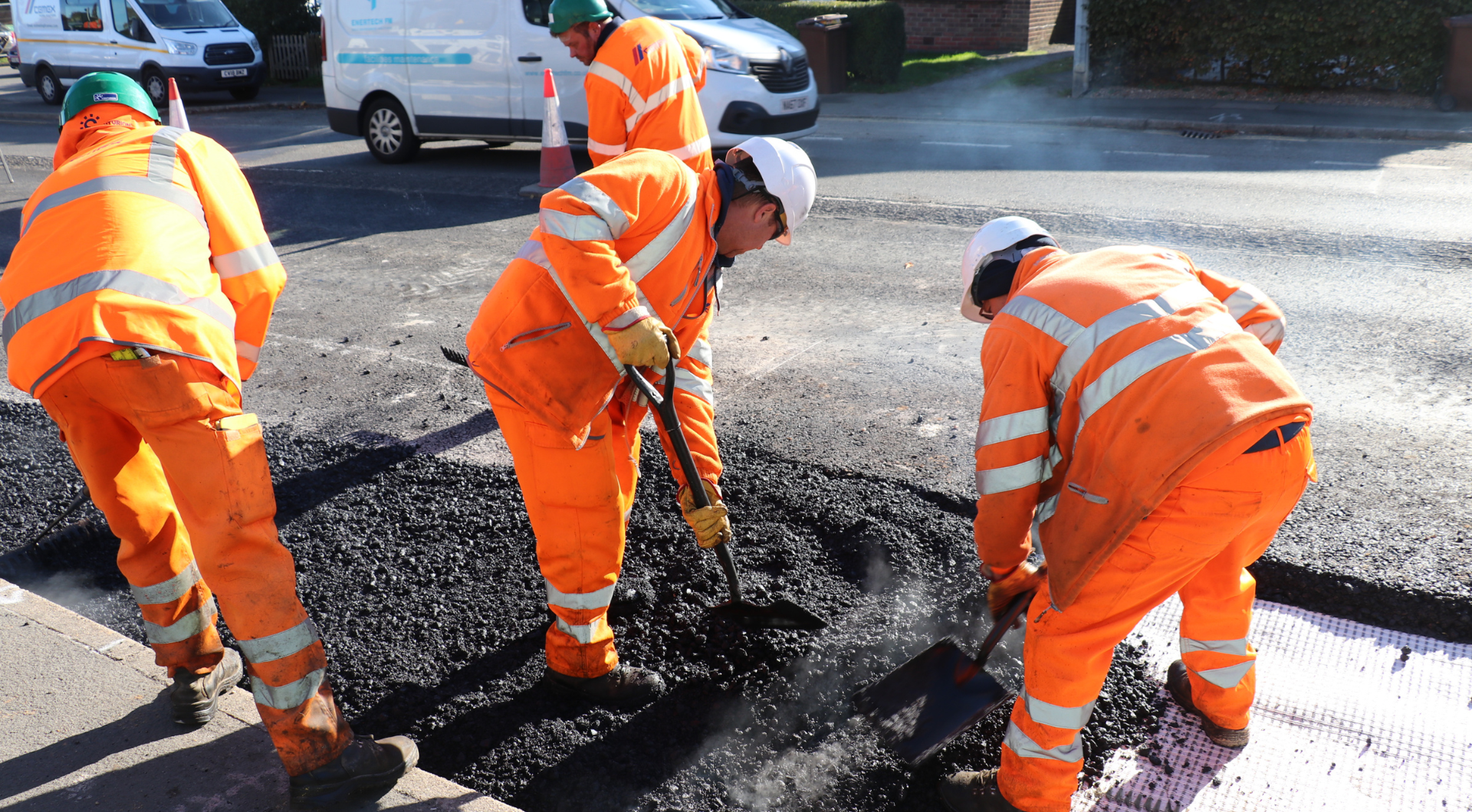 Three workmen in high vis wear filling a pothole in the road.