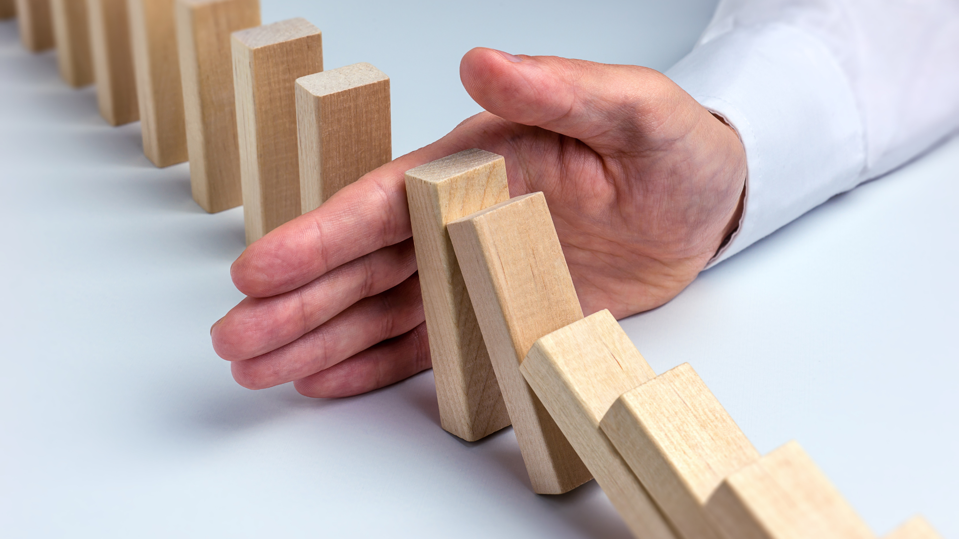 A hand stops a row of dominoes from falling