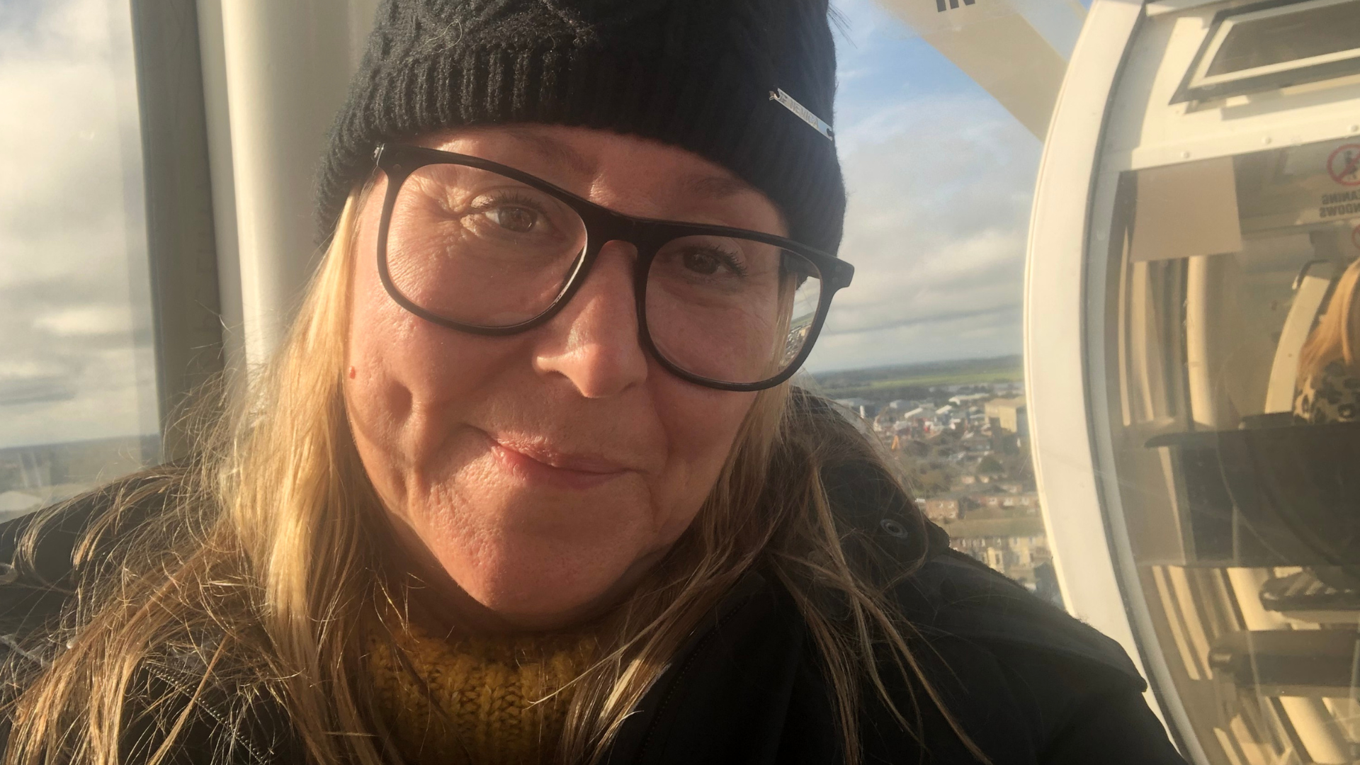 A woman taking a selfie wearing glasses and a wooly hat and coat.